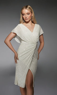 A woman poses in a studio with one hand on her hip, wearing the Alyce 70063 knee-length semi-formal dress in Diamond White, featuring short sleeves, a v-neckline, sequins, and a draped faux-wrap front.