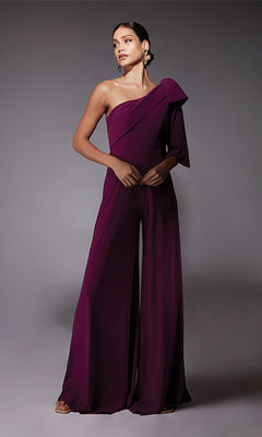 A woman wears the Alyce 70065 Long Formal Jumpsuit in Sparkling Grape—sleeveless, wide-leg, one-shoulder with a large bow—standing against a plain gray background, offering a chic alternative to a cocktail dress.