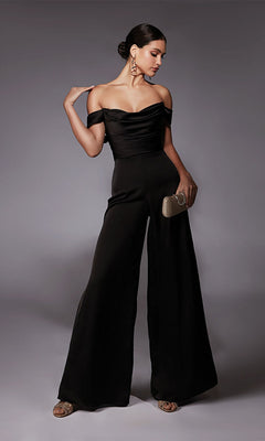 Woman poses against a plain gray background wearing the Alyce 70071 long formal off-shoulder satin jumpsuit with wide-leg pants, gold heels, statement earrings, and holding a gold clutch.