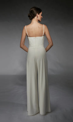 A woman wears the Alyce 70075 Long Formal Jumpsuit, featuring a sleeveless, corset-boned bodice and wide legs. She styles her hair in a low bun and completes the look with long earrings.