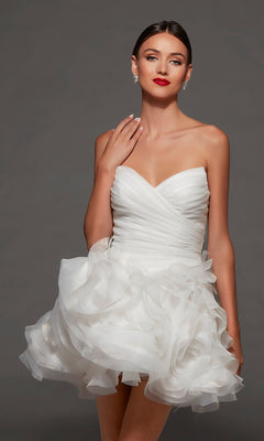 A woman wearing the Alyce 70086 short white party dress, featuring a strapless sweetheart neckline and ruffled skirt, accessorized with red lipstick and earrings, poses against a plain gray background.