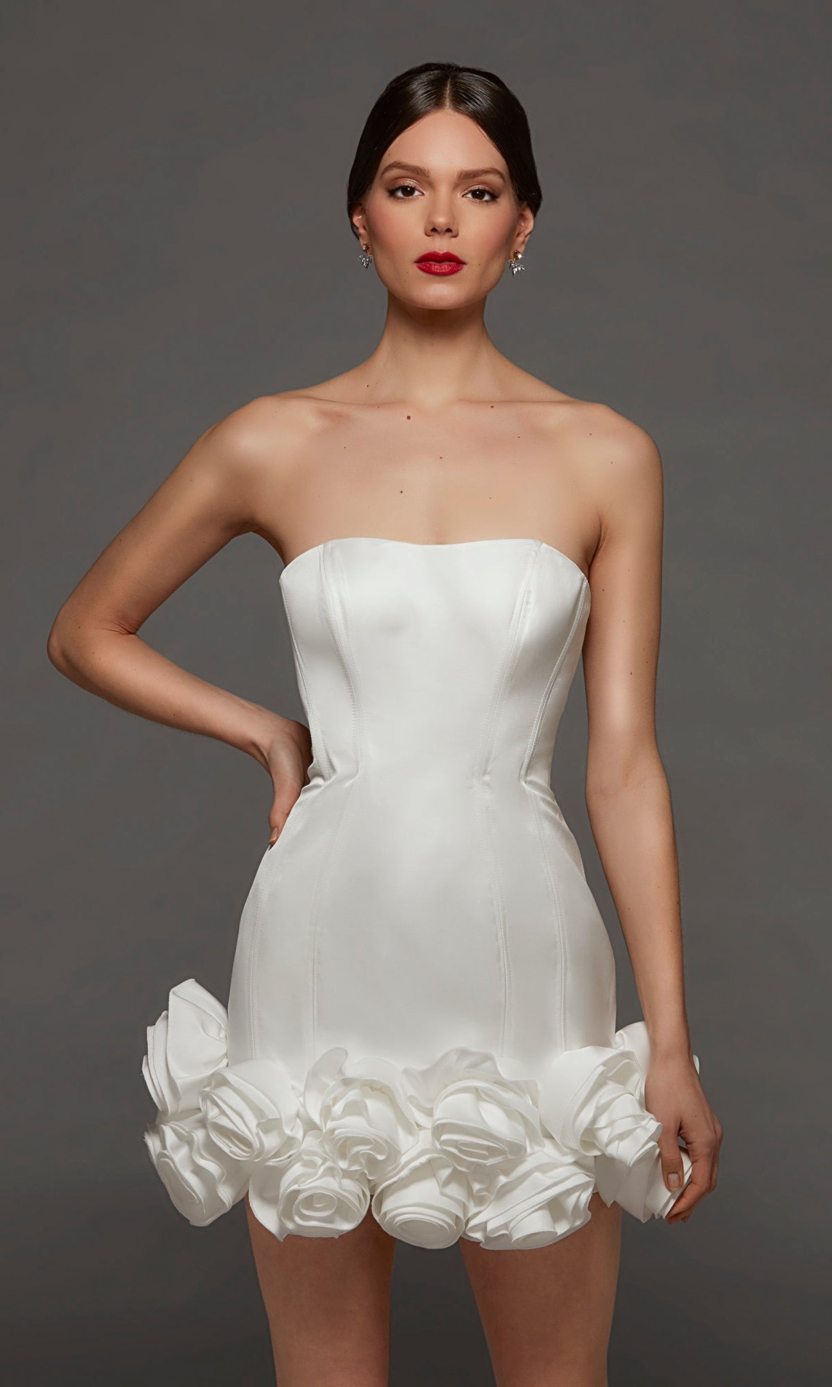 A woman poses against a plain gray background wearing the Short White Party Dress: Alyce 70087 in Diamond White—a strapless bodycon mini dress featuring rose-shaped fabric decorations along the rosette hemline.
