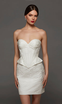 A woman wearing the Short White Party Dress: Alyce 70093, featuring a strapless sweetheart neckline with a structured corset bodice and textured skirt, stands against a plain gray background.