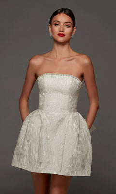A woman wearing the Alyce 70097 short white party dress in diamond white, a strapless jacquard mini dress with pockets, stands against a plain gray background and looks directly at the camera.