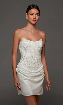 A woman wearing the Alyce 70105 short white party dress, which features a sparkling corset bodice and draped satin skirt, stands against a plain gray background.
