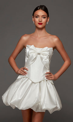 A woman stands against a plain gray background, wearing the Alyce 70108 short party dress in diamond white—a strapless corset design with shiny fabric, a large bow accent on the bodice, and a voluminous bubble-hem skirt.