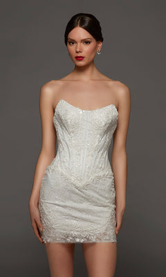 A woman wearing the Alyce 70116 Short White Party Dress in Diamond White, featuring a strapless, fitted silhouette with delicate lace detailing and a flattering corset bodice, stands against a plain dark background.