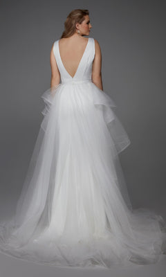 A woman wearing the Alyce 7019 long white dress—a sleeveless bridal gown with a deep V-back and layered tulle skirt—stands against a gray background, facing away from the camera.