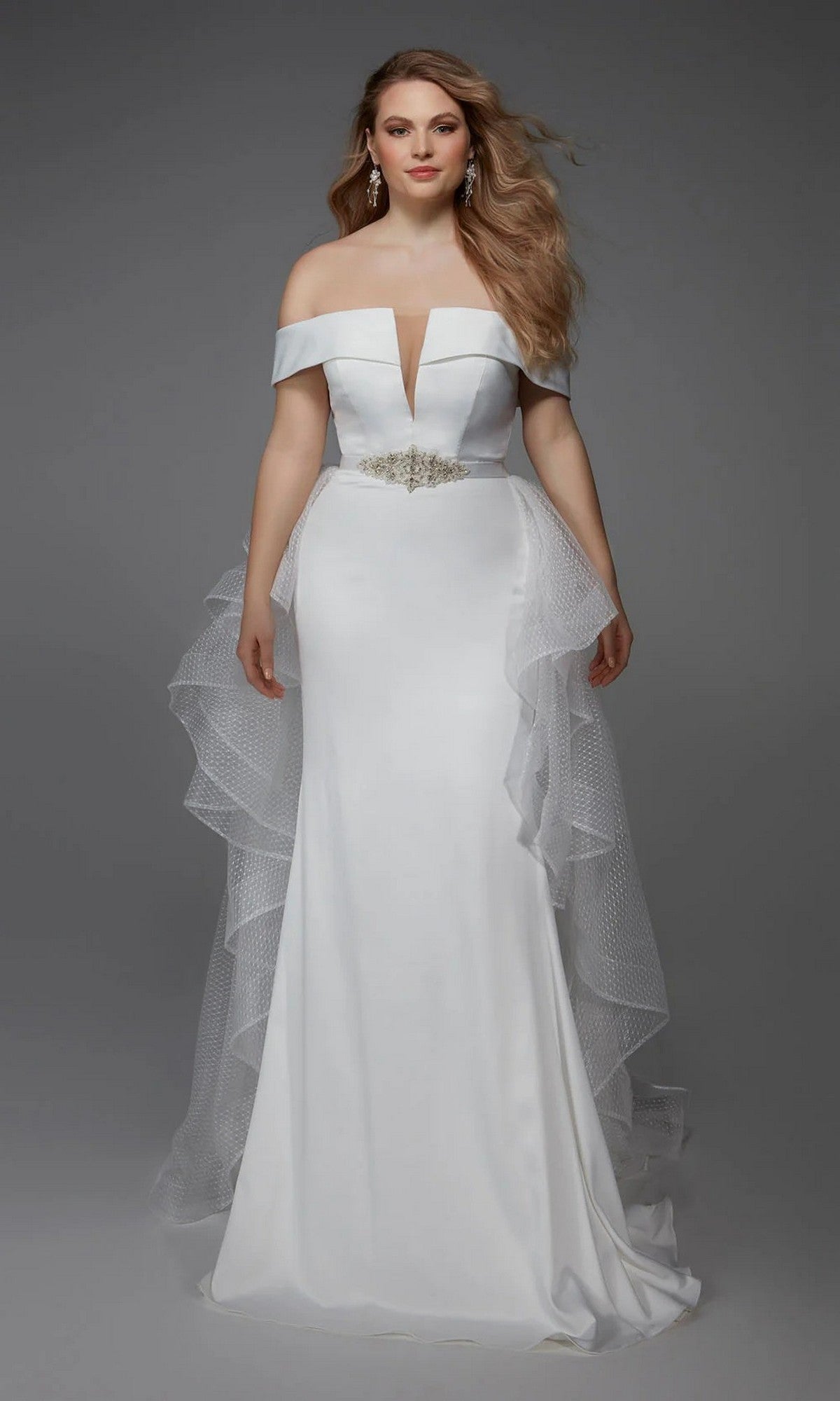 A woman wears the Alyce 7020 Long White Dress—a satin off-the-shoulder gown with a fitted bodice, deep V neckline, beaded belt, and layered tulle hip accents—ideal for bridal events or elegant wedding receptions.