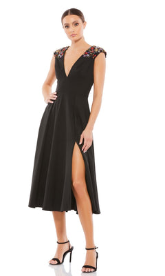 A woman wears the Short Wedding Guest Dress 70214 by Mac Duggal: a sleeveless black v-neck A-line dress with floral-embellished shoulders, thigh-high slit, and paired with black high-heeled sandals.