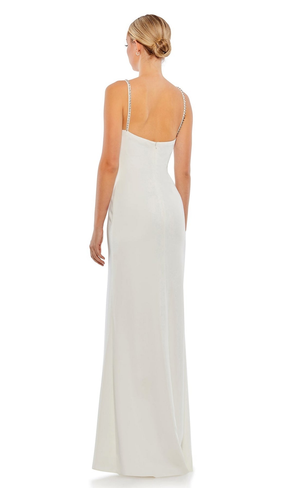 A woman in a white, floor-length v-neck Long Formal Dress 70220 by Mac Duggal with beaded straps and a low back stands facing away, elegantly showcasing the gown’s stunning back detail.