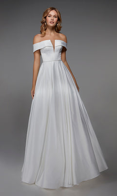 A woman models the Alyce 7023 Long White Dress in Diamond White, featuring an off-the-shoulder fitted bodice and a full, floor-length skirt, standing before a plain gray background.