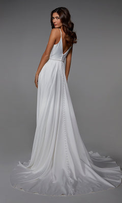A woman models the Alyce 7024, a sleeveless white satin floor-length formal dress with an A-line skirt, deep V-back, and button detail, standing against a neutral background.