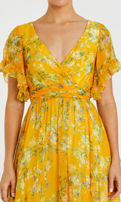 A woman wearing the Floral-Print Long Formal Dress 70241 by Mac Duggal, featuring a yellow Bohemian floral print, short ruffled sleeves, V-neckline, and fitted waist.