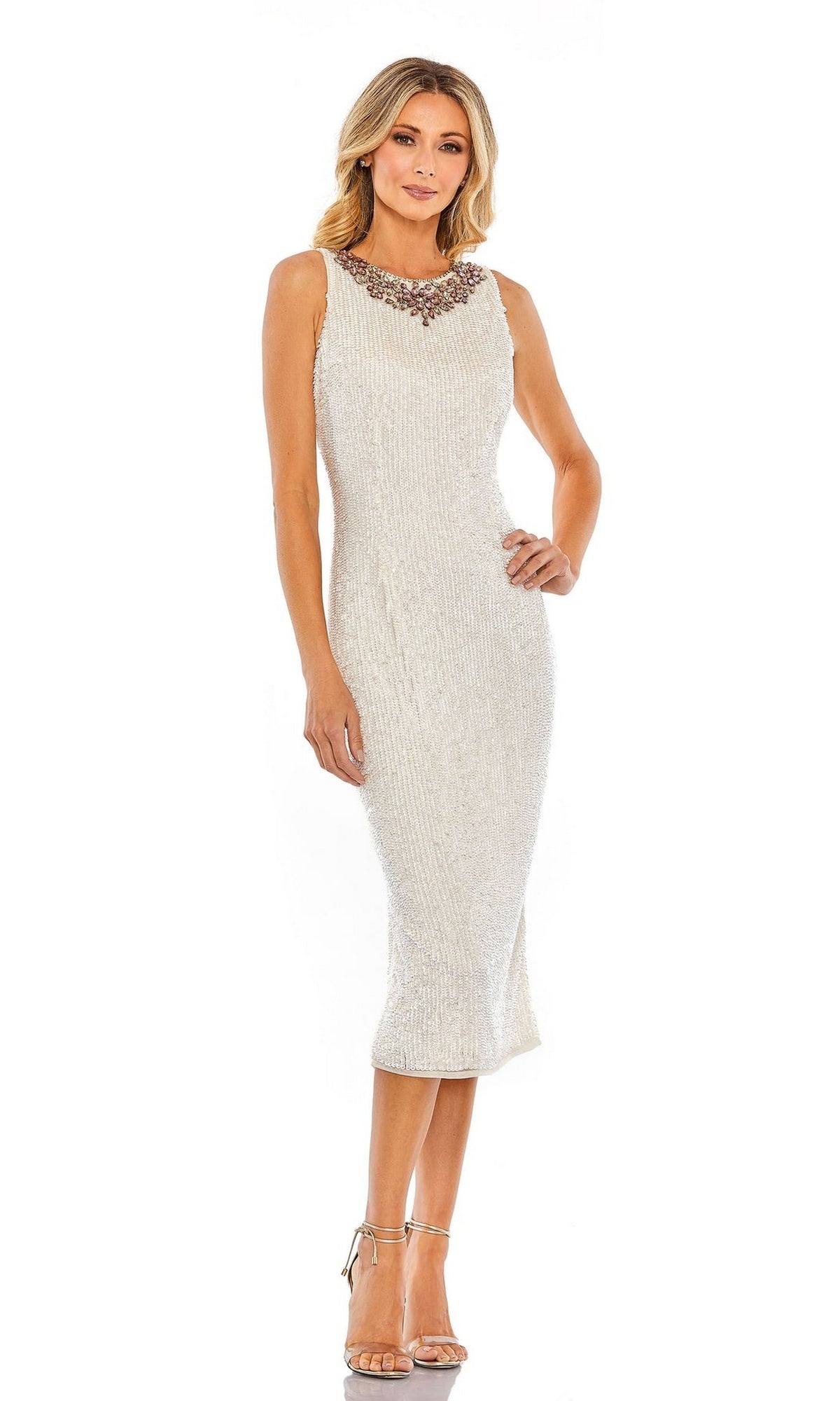 A woman in the Short Party Dress 70269 by Mac Duggal—white, sequined, sleeveless with a beaded high neckline—pairs it with silver heels and poses against a white background.