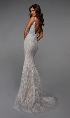 A woman poses in the Alyce 7028 long white dress, a fitted, floor-length evening gown with lace embroidery, a train, and backless design, shown against a plain gray background.