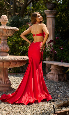 A woman wearing the Long Halter Prom Dress: Atria 7034H stands outdoors by a stone fountain and bench, looking over her shoulder with a smile.