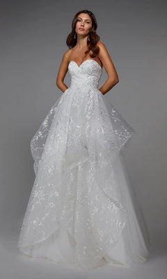 A woman models the Alyce 7041 long formal dress in ivory, featuring a strapless tulle ball gown design with floral lace details and a voluminous layered skirt, against a plain grey background.