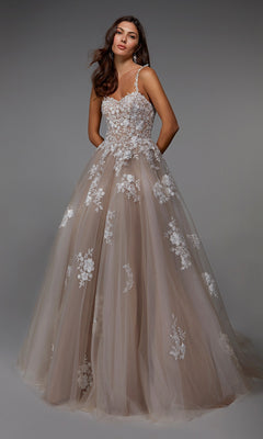 A woman poses gracefully against a plain gray background wearing the Alyce 7043, a long formal blush tulle ballgown with white floral lace appliqué and thin straps.
