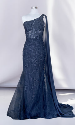 The One-Shoulder Long Lace Mermaid Prom Dress 7048 in navy blue features floral embroidery, sheer detailing, and a long draped sash, elegantly showcased on a dress form.