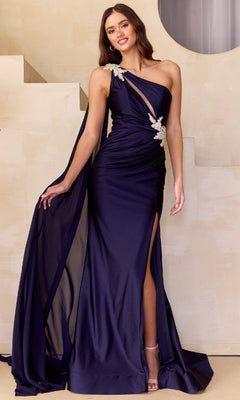 A woman in the Amelia Couture 7056—a navy blue, one-shoulder long prom dress with silver floral accents, draping fabric, and a thigh-high slit—stands before a beige geometric backdrop: elegance meets affordability.