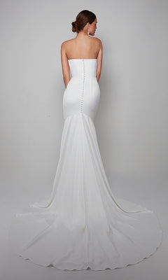 Woman wearing the Alyce 7057 long white dress, featuring a strapless design, button details down the back, and a flowing train, standing against a plain background.
