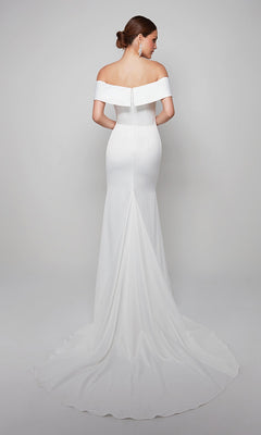 A woman in the Long White Dress: Alyce 7059—an off-shoulder, fitted gown with a flowing long train—stands facing away against a plain light background.