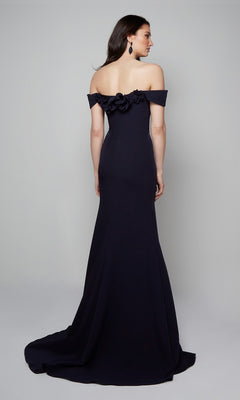 A woman wears the Alyce 7062 Long Formal Dress with an off-the-shoulder neckline and 3D floral back accents, posed against a plain light gray background.