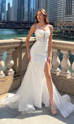 Woman in an Amelia Couture 7064 Long Mermaid Prom Dress with a sheer bodice and high slit stands on a stone terrace by a river, exuding elegance like a floral lace gown amid tall urban buildings.