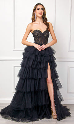 A woman exudes evening elegance in the Amelia Couture 7067 Strapless Ruffled Prom Gown, featuring a tiered tulle skirt and thigh-high slit, as she stands against a white paneled wall.