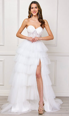 A woman in the Amelia Couture 7067 Strapless Ruffled Prom Gown with a tiered tulle skirt and thigh-high slit stands indoors against a white paneled wall.