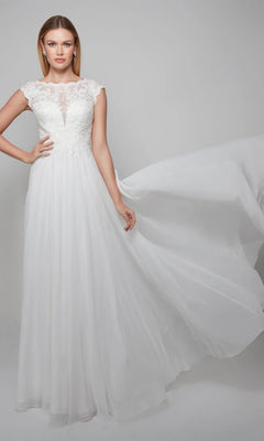 A woman models the Long White Dress: Alyce 7073 in Diamond White, featuring lace embroidery and a chiffon A-line skirt, as she holds out one side of the flowing skirt against a plain light background.