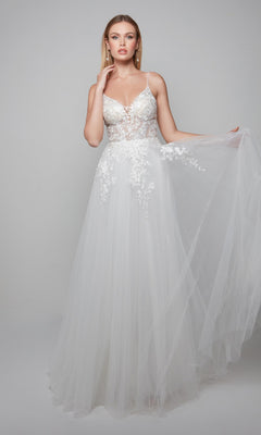 Radiating bridal elegance, she wears the Alyce 7079 long white dress featuring floral lace on the bodice and a sheer tulle skirt, standing against a plain background.