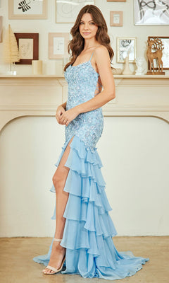 A woman in the Amelia Couture 7085 Ruffled Long Prom Dress, light blue with an embroidered bodice and high slit, stands sideways by a decorated mantel featuring framed art and small sculptures.