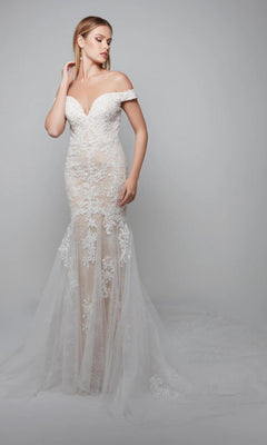 A woman in the Alyce 7086 long ivory dress with floral lace appliques and a sheer tulle skirt stands against a plain gray background.