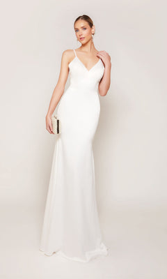 A woman in the Alyce 7090 Long Formal Dress, featuring a sleeveless, floor-length design in diamond white with thin straps, holds a small clutch against a plain light background.