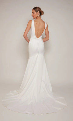 A woman in the Alyce 7091 long white dress—sleeveless with a plunging V-neckline, deep V-back, button accents, and a long train—stands against a plain light background.
