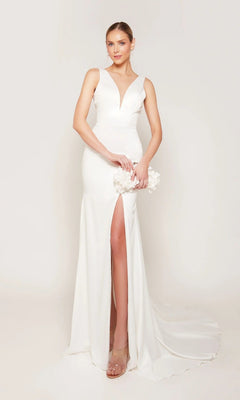 Wearing the Alyce 7091 long white dress with a sleeveless plunging V-neck, thigh-high slit, and train, a woman holds a white floral clutch against a plain light background.