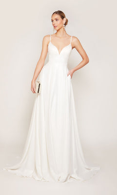 A woman stands against a plain light background wearing the Alyce 7095 long white dress, featuring satin fabric, thin straps, and a V-neckline. She holds a small clutch in one hand.