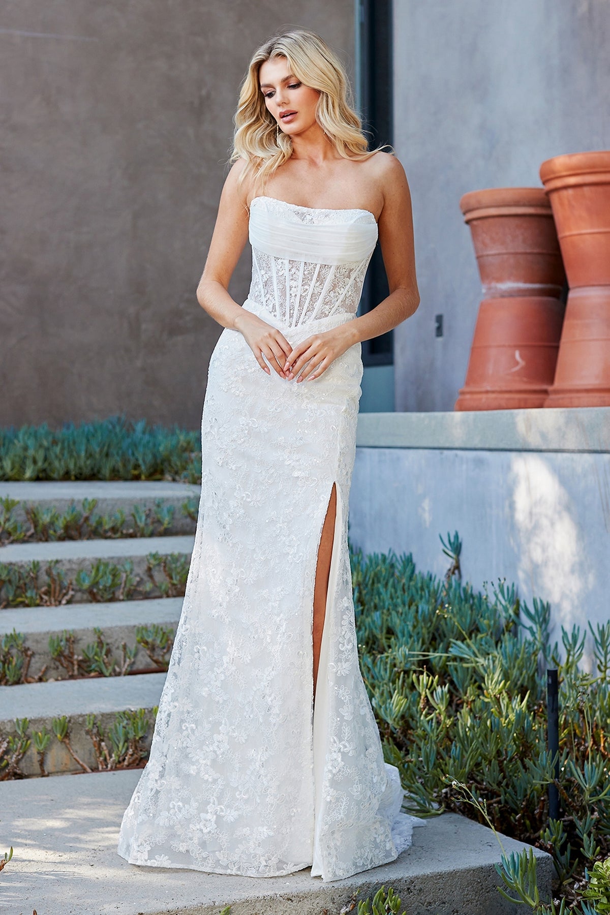 Long Prom Dress: Amelia Couture 7097 is a floor-length, strapless white lace gown featuring a corset-style bodice and a high side slit.