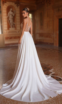 A woman wearing the Alyce 7099 long white dress with beaded spaghetti straps and an open back stands in an ornate room with classical decor and a marble floor.