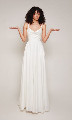 A person with curly hair models the Alyce 7100 long formal dress, standing with arms raised and palms up against a plain background.