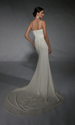 A woman stands facing away in the Alyce 7103, a fitted long white dress with thin straps, a long train, and button details down the back, highlighting the gown’s elegant formal style.