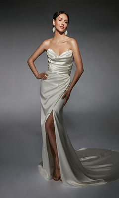 A woman poses against a dark background wearing the Alyce 7106, a long white strapless satin gown featuring a cowl neckline, thigh-high slit, and subtle train.