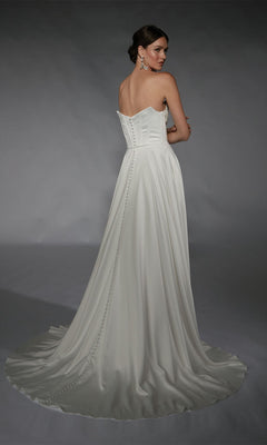 A woman poses elegantly in a studio with a gray background, wearing the Alyce 7110: a long white strapless formal gown with button details and a train.