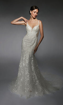A woman poses in the Alyce 7122, a fitted long white dress featuring thin straps and a sheer train adorned with floral lace appliqués.