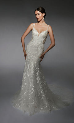 A woman stands against a dark background wearing the Long White Dress: Alyce 7122—a sleeveless wedding gown with a fitted bodice, v-neckline, thin straps, floral lace appliqués, and a long flowing train.