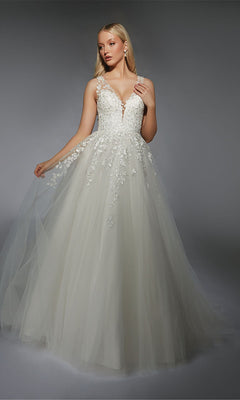 A woman models the Alyce 7128 Long White Dress, featuring delicate lace appliqué and a flowing tulle skirt, set against a plain gray background.