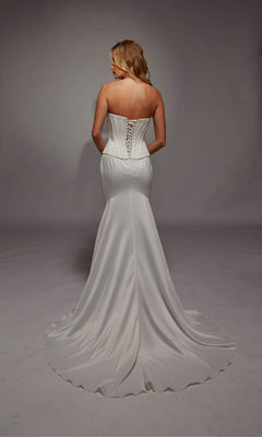 A woman wears the Alyce 7136 long white dress, featuring a strapless satin corset bodice, lace-up back, and sweep train, as she stands with her back to the camera.