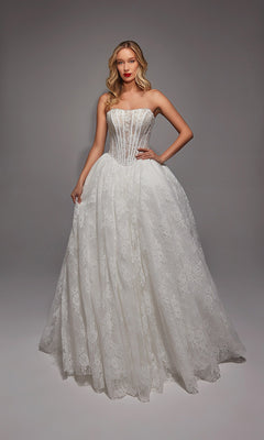 A woman stands in a studio wearing the Long White Dress: Alyce 7149 in Ivory/Sand, featuring a strapless fitted bodice, delicate lace, and full skirt, with one hand on her hip.